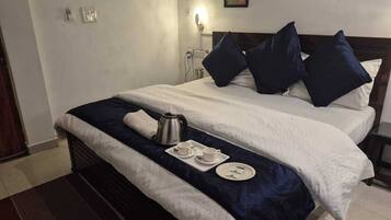 Quarto de hotel com duas camas, um cobre-leito azul escuro, lençóis brancos e uma bandeja com chaleira, chávenas e um prato.