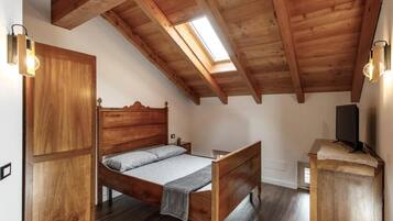 Un dormitorio con una cama de madera, una mesita de noche, un televisor sobre un soporte de madera y un tragaluz.