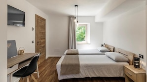 Une chambre avec un bureau, deux lits, une télévision et une fenêtre avec des rideaux.