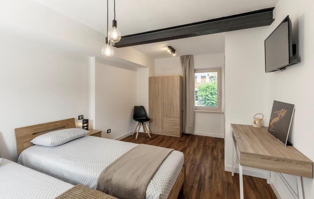 A modern hotel room with two beds, a desk, a TV, and a view of the outdoors.