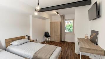 A modern hotel room with two beds, a desk, a TV, and a view of the outdoors.