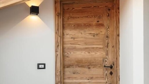 Une porte en bois surmontée d’un luminaire moderne, un petit interrupteur sur le mur et un plancher en bois foncé.