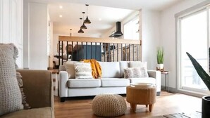 Ein modernes Wohnzimmer mit Sofa, Hocker und Couchtisch. Eine Treppe führt zu einer oberen Ebene.