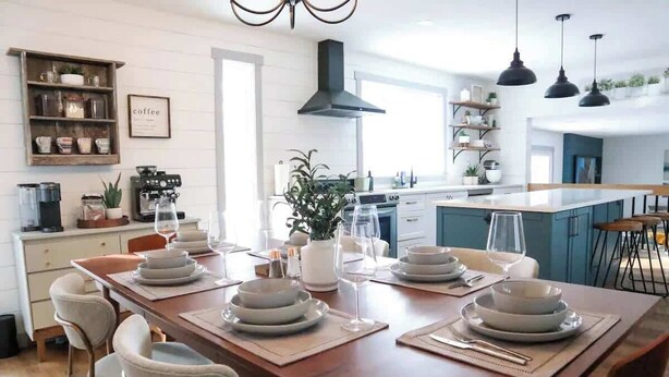 Eine moderne Küche mit einer zentralen Kochinsel, einem Holzespeisetisch für vier Personen und einer Kaffeestation.
