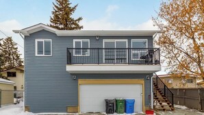 A two-story house with a garage, a balcony, and a staircase leading to the upper floor. There are three trash bins in front of the garage. - AC, 95 min Banff, Local Coffee,Walk to Restaurants (Calgary)