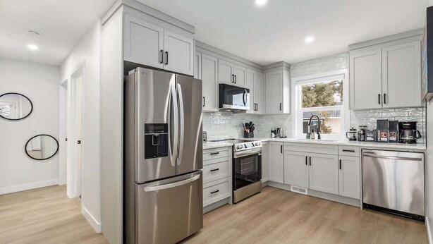 A modern kitchen with stainless steel appliances, white cabinetry, and a wooden floor. - AC, 95 min Banff, Local Coffee,Walk to Restaurants (Calgary)