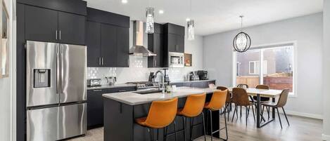 A modern kitchen with dark cabinets, stainless steel appliances, and a central island with orange bar stools.