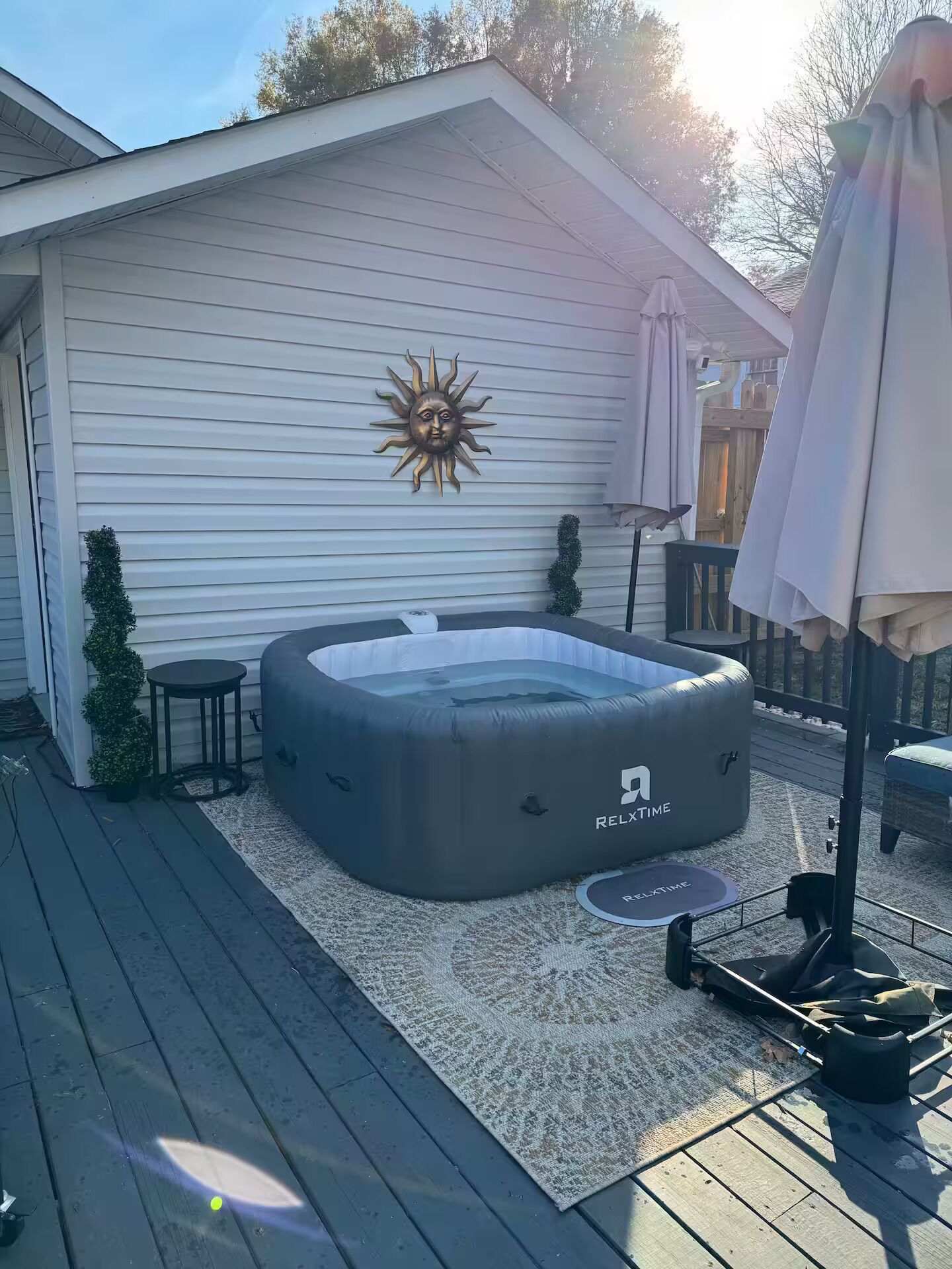 Un bain à remous sur une terrasse en bois, avec une maison blanche en arrière-plan.
