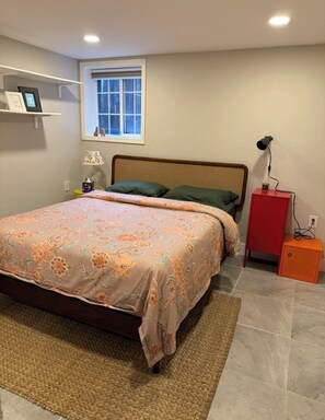 A bedroom with a bed, a nightstand, a lamp, a window, and a shelf with pictures. - Beautiful condo - WALK to Oakland’s best offerings ! (Oakland)
