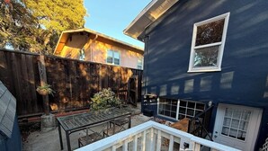 Un patio trasero con cerramiento de madera, una mesa de metal y una casa azul.