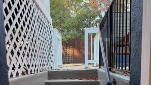 Un conjunto de escalones de hormigón que conducen a una puerta blanca, rodeada por un enrejado y un portón metálico.