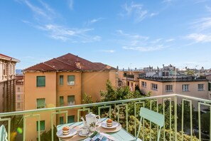 Ein Balkon mit einem für Tee gedeckten Tisch, mit Blick auf eine Wohngegend mit Gebäuden und Grünflächen.