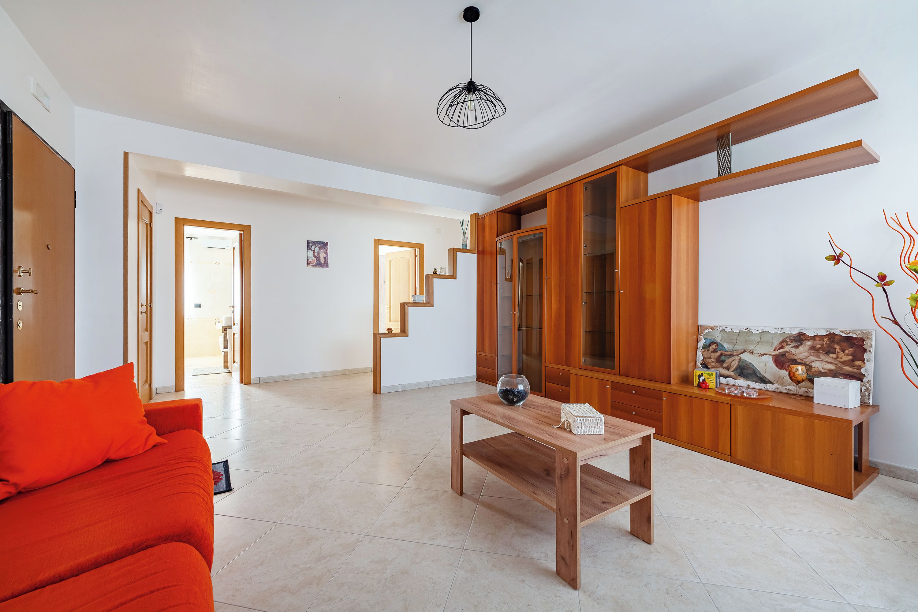 Uma sala de estar moderna com uma mesa de centro de madeira, um sofá vermelho e uma escada que leva a outro cômodo.