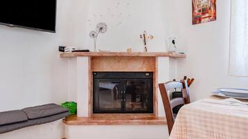 Una sala de estar con chimenea, un televisor de pantalla plana montado en la pared y un comedor con mesa preparada para dos.