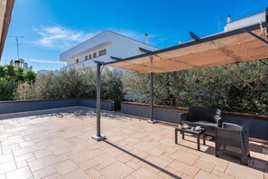 An outdoor patio area with a covered seating area, a tiled floor, and a view of a white building with multiple windows. - Bianca Olive House - Alberobello (Alberobello)