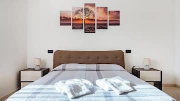 Un dormitorio con una cama, dos mesitas de noche, un cuadro de un árbol en la pared y una manta sobre la cama.