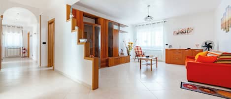 A spacious living room with a red sofa, wooden cabinets, and a dining area with a table and chairs.