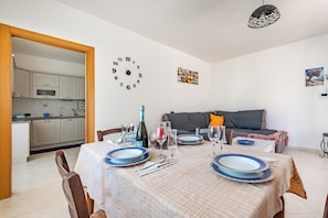 A dining area with a table set for four, a kitchen in the background, and a wall clock. - Bianca Olive House - Alberobello (Alberobello)