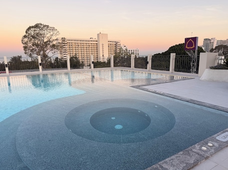 A swimming pool with a circular design, surrounded by a fence and a building in the background.. Aston Hotel Pattaya