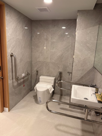A modern bathroom with a toilet, bidet, and sink, equipped with grab bars and a shower chair.. Aston Hotel Pattaya