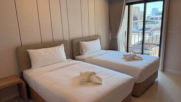 Habitación de hotel con dos camas, una mesita de noche y un ventanal con vistas a la ciudad.