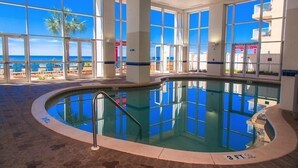 Une piscine intérieure offrant une vue dégagée sur l’océan et les palmiers grâce à de grandes fenêtres.