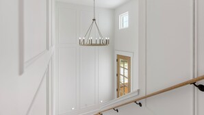 Una escalera con barandilla de madera, paredes blancas y un candelabro.