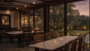 A dining area with a large table and chairs, wooden beams on the ceiling, and large windows overlooking a garden. - Silvanza Resort By Nivanta (Ramnagar)
