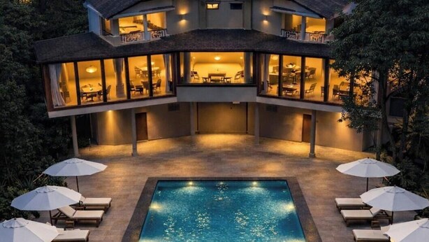 A modern two-story house with a swimming pool, lounge chairs, and umbrellas. - Silvanza Resort By Nivanta (Ramnagar)
