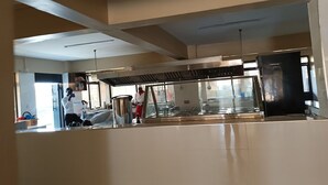 A kitchen area with stainless steel appliances, a large window, and a person in a chef's uniform. - Silver Brooke Hotel Othaya (Othaya)
