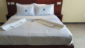 A neatly made bed with white linens and two pillows, a wooden headboard, and a bedside table with a power outlet. - Silver Brooke Hotel Othaya (Othaya)