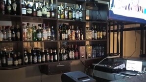 A bar area with shelves of liquor bottles, a television screen, and a laptop on a counter. - Silver Brooke Hotel Othaya (Othaya)