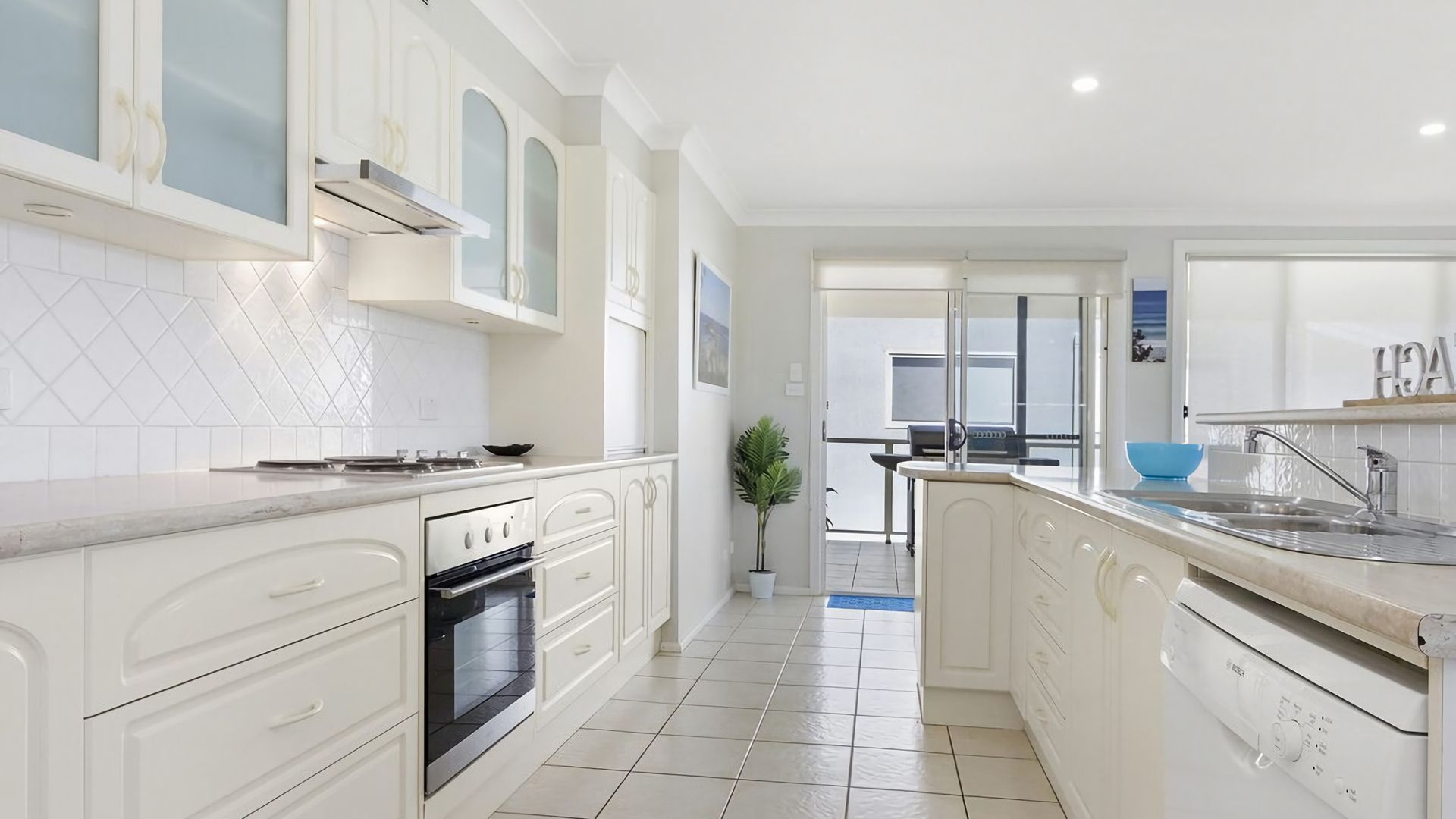 Une cuisine moderne avec des meubles blancs, un four encastré et un grand îlot central doté d’un évier.
