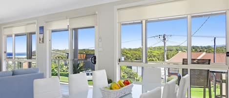 A modern living room with a dining area, large windows, and a view of the outdoors.