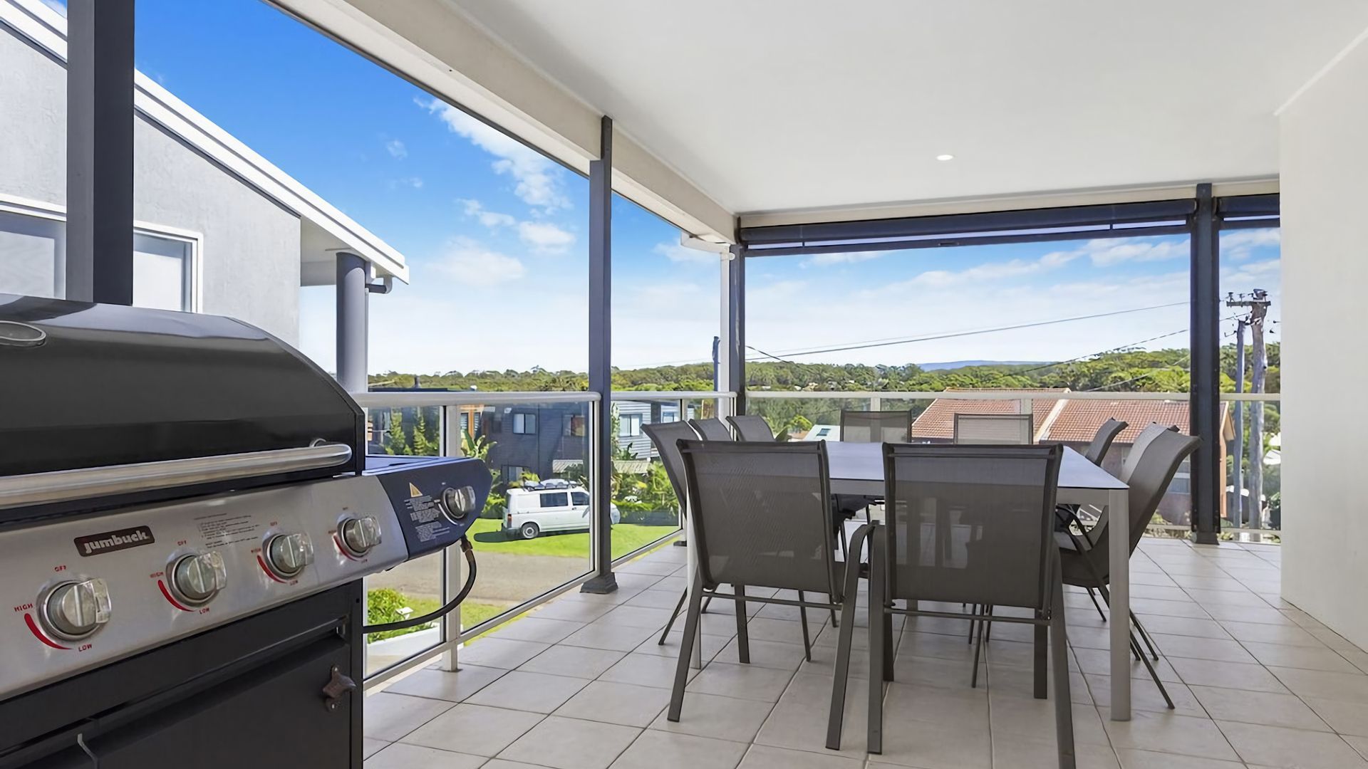 Ein Balkon mit Grill, Esstisch und Stühlen mit Blick auf eine Wohngegend.
