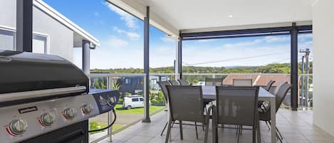 Ein Balkon mit Grill, Esstisch und Stühlen mit Blick auf eine Wohngegend.