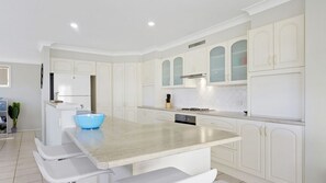 A modern kitchen with white cabinetry, a central island with a blue bowl, and a built-in dishwasher. - Sea-Renity is a spacious home (Manyana)
