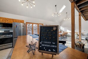 Ett modernt kök med rostfria vitvaror, en köksö i trä och en griffeltavla där det står ett välkomstmeddelande till gästerna.