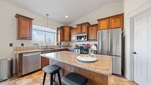 Una cocina moderna con armarios de madera, electrodomésticos de acero inoxidable, encimera de granito y una isla integrada con taburetes de bar.