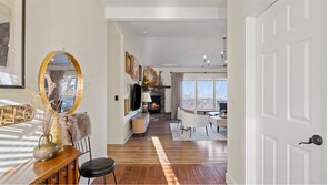 Un vaste salon doté d’une cheminée, de parquet et d’un coin repas avec des chaises blanches.
