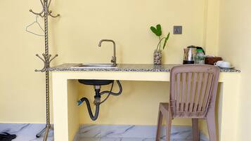 A compact kitchen with a sink, a chair, a coat rack, and a small plant on the counter.