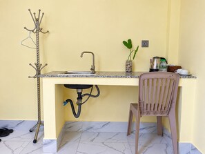 A compact kitchen with a sink, a chair, a coat rack, and a small plant on the counter. - AHHA River Breeze Kampot  (Kampot)