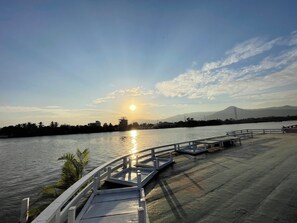 Une jetée en bois s’étendant au-dessus d’une étendue d’eau calme, sous un ciel dégagé, avec des montagnes lointaines à l’horizon.