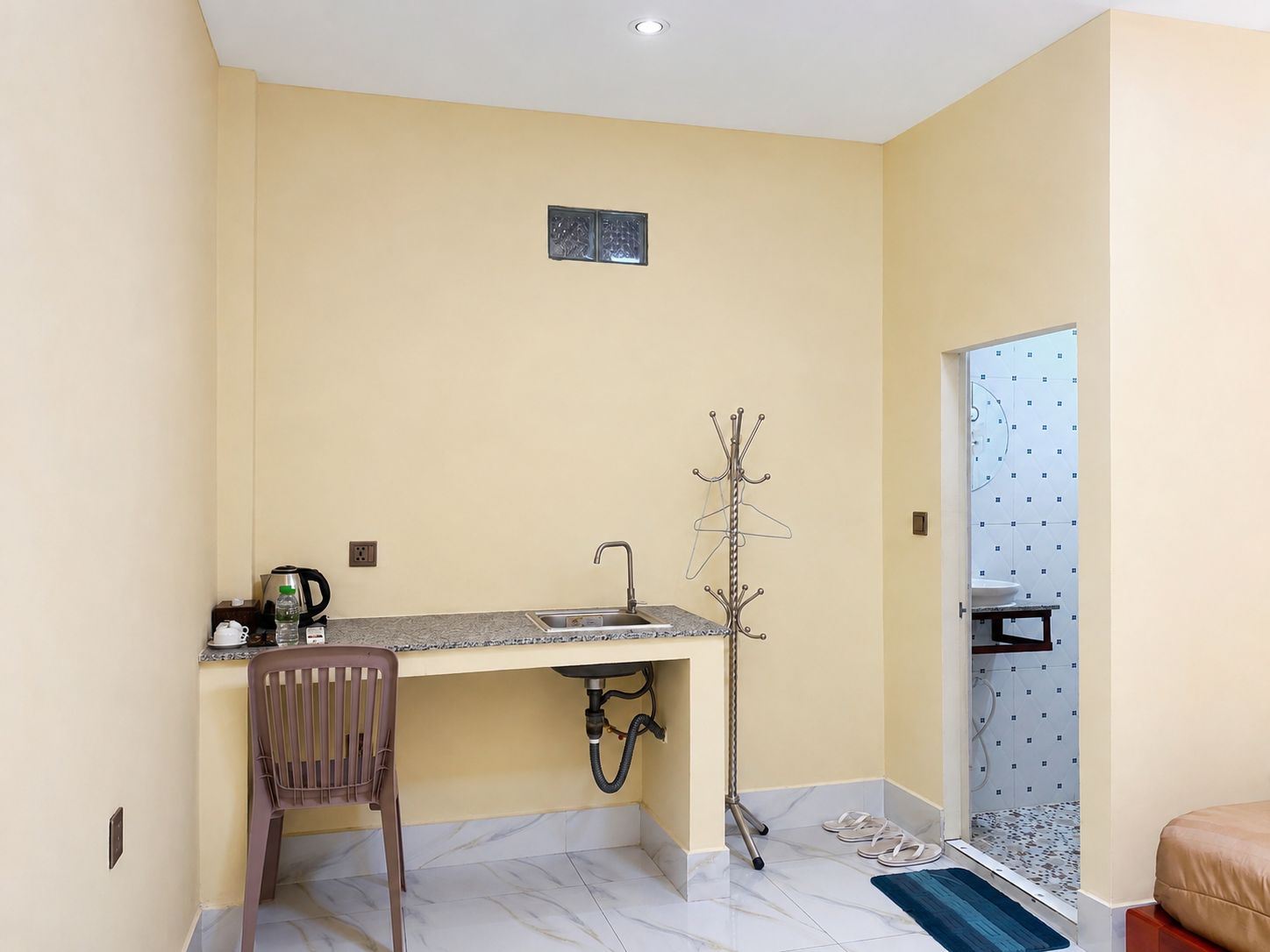 A compact room with a kitchenette, a coat rack, a chair, and a bathroom with a toilet and sink.