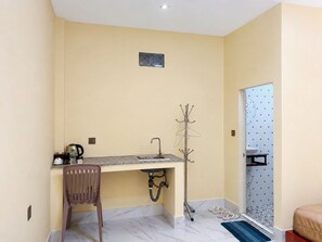A compact room with a kitchenette, a coat rack, a chair, and a bathroom with a toilet and sink. - AHHA River Breeze Kampot  (Kampot)