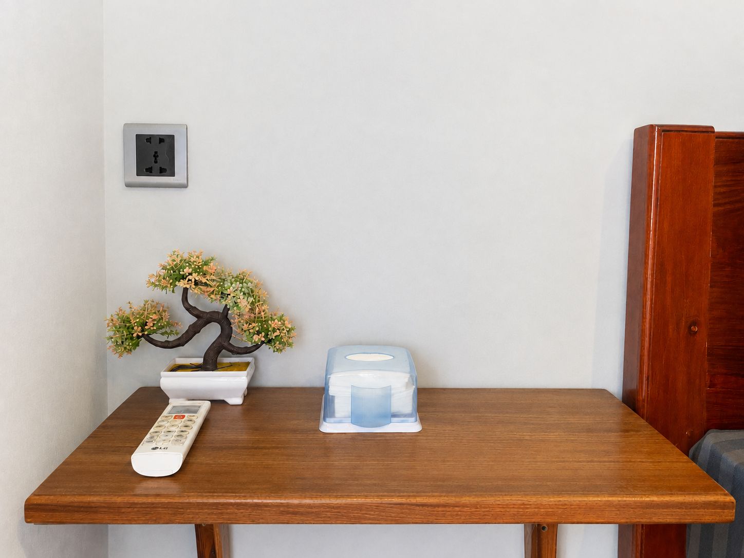 A wooden table with a remote control, a small bonsai tree, and a tissue box.