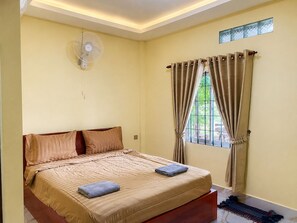 A bedroom with a bed, a standing fan, a window with curtains, and a small skylight. - AHHA River Breeze Kampot  (Kampot)