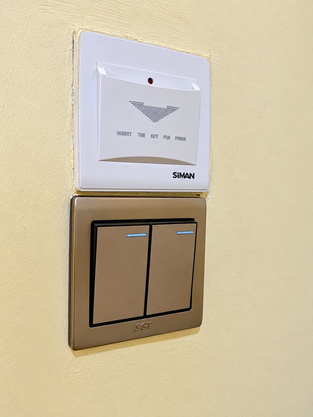 Een bedieningspaneel aan de muur, met een keypad van SIMAN en een schakelaar van SGT.