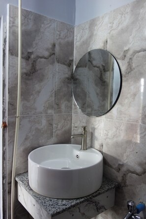 Een badkamer met een wit wastafelmeubel, een ronde spiegel en marmeren wanden.