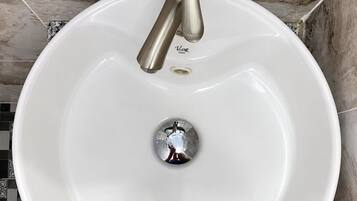 Un lavamanos blanco con un solo grifo, sobre un piso de baldosas con diseño geométrico.